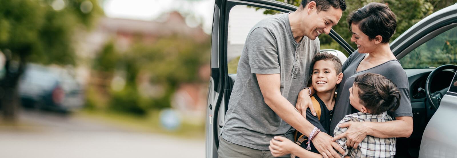 A young family embracing next to a car
