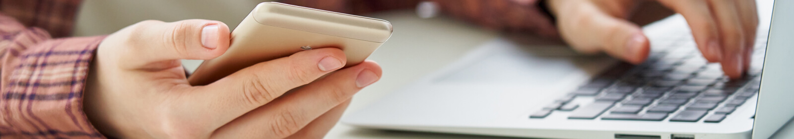 Close up of a person's hands holding a smartphone and using a laptop