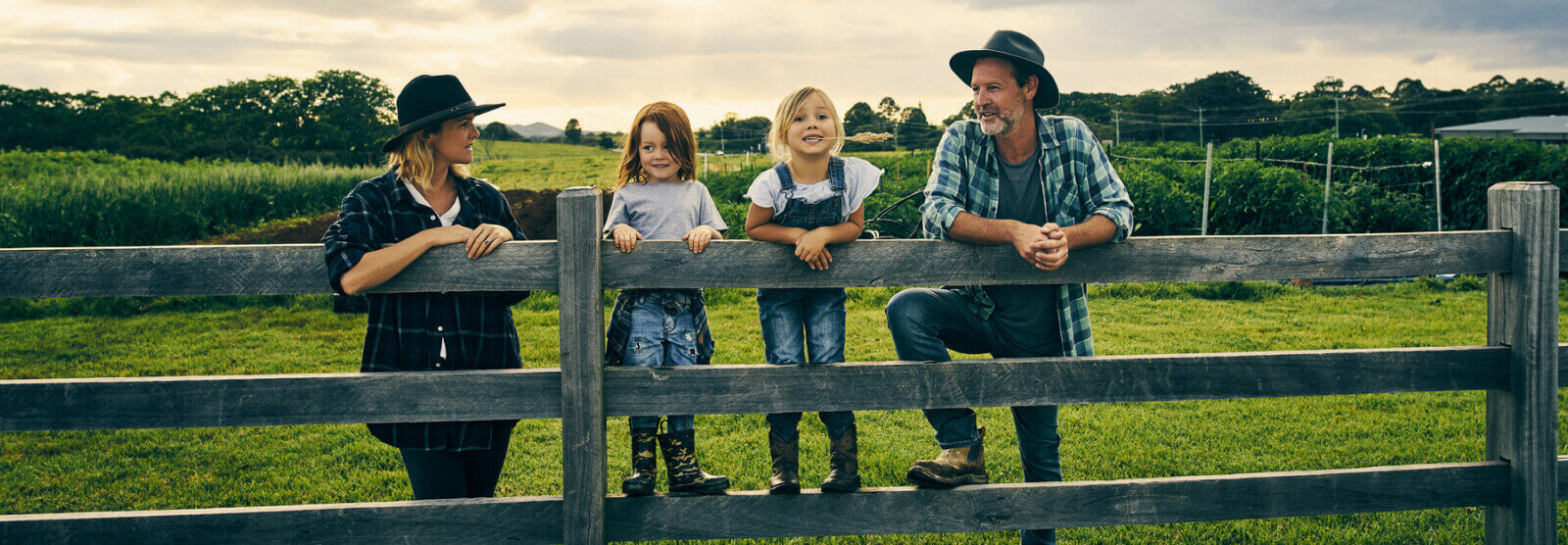 A young family standing on a fence outside in a rural area